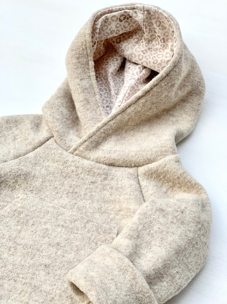 May include: A beige hooded sweatshirt with a leopard print lining. The sweatshirt is made of a soft, fuzzy fabric.