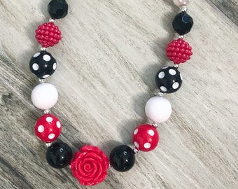 May include: A red, white, and black beaded necklace with a red rose charm. The necklace is made of large, chunky beads with polka dots.