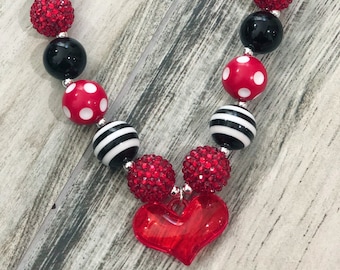 May include: A red, black, and white beaded necklace with a red heart charm. The beads are various sizes and shapes, including polka dots, stripes, and rhinestones.