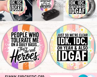 Puede incluir: Un juego de dos posavasos redondos para coche con textos humorísticos. Uno dice "JUST SO WE'RE CLEAR IDK, IDC, OH YEAH & ALSO IDGAF" y el otro "PEOPLE WHO TOLERATE ME ON A DAILY BASIS... They're the real Heroes."