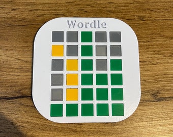 May include: A white plastic game board with the word "Wordle" printed on it. The board has a grid of 30 squares, with 5 rows of 6 squares each. The squares are colored gray, yellow, and green.