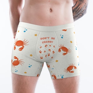 May include: White boxer shorts with a repeating pattern of orange crabs, blue dots, and yellow stars. The waistband features the text "DON'T BE CRABBY" in orange. The underwear is made of a soft, comfortable material.