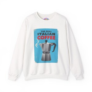 May include: White sweatshirt featuring a graphic of a silver Italian coffee maker on a blue background. The text "THE REAL ITALIAN COFFEE" is printed above the coffee maker in red and white. The sweatshirt has a crew neck and long sleeves.