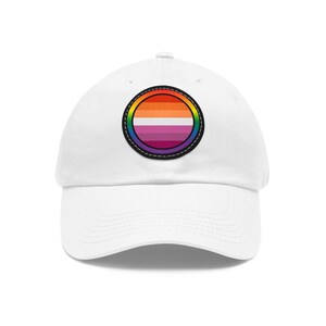 Könnte beinhalten: Weiße Baseballkappe mit einem runden Patch in Regenbogenfarben und pinken, weißen und orangen Streifen.