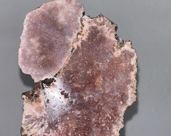 May include: A pink and brown agate slice on a black stand. The agate has a natural, organic shape and a polished surface.