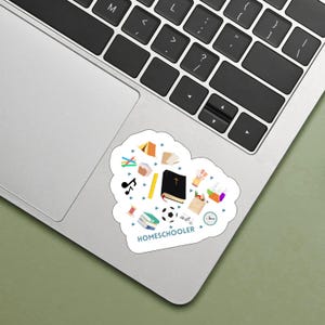 May include: A white heart-shaped sticker with a blue border and the text "Homeschooler" at the bottom. The sticker features various colorful illustrations of school supplies, including books, a ruler, a soccer ball, a clock, a tent, a Bible, and a musical note.