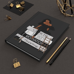 May include: A black journal with the words "Growth, Money, Motivation, Happiness" printed on the cover. The journal features an illustration of a woman in a black dress sitting on a stack of books. Gold and black pencils and binder clips are also visible.