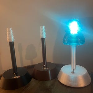 May include: Three decorative lamps with a unique design. Each lamp features a base in black, brown, and white, supporting a central stem and a light fixture. One lamp is illuminated with a bright blue light, while the others are unlit.