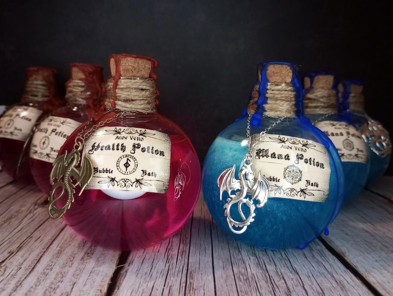 May include: Two glass potion bottles, one filled with pink liquid and the other with blue liquid. Each bottle has a cork stopper, twine, and a decorative label. A dragon charm hangs from each bottle. The labels read "Health Potion" and "Mana Potion".