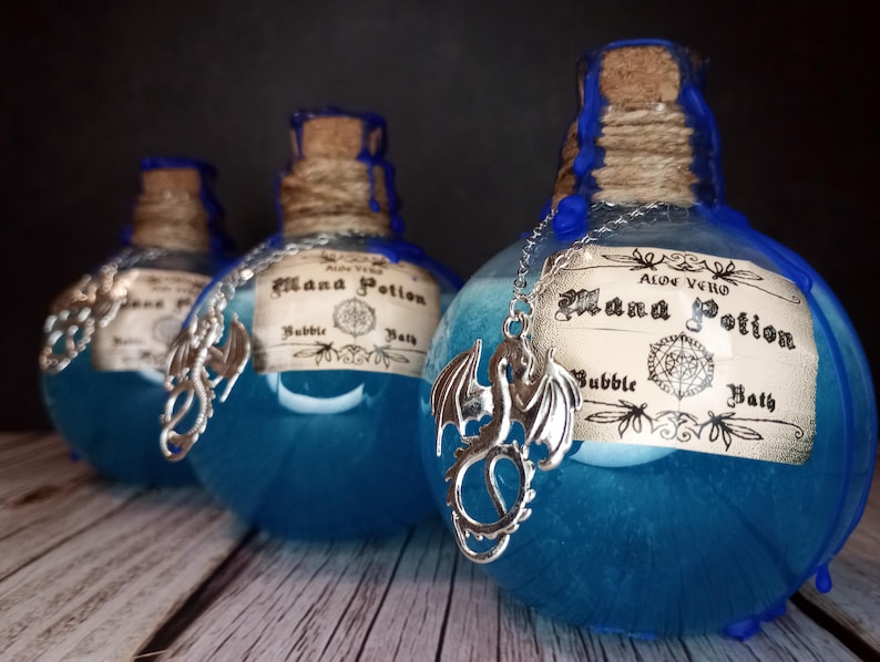 May include: Three blue glass bottles with cork stoppers and silver dragon charms. Each bottle has a label that reads "Mana Potion Bubble Bath". The bottles are filled with a blue liquid and are decorated with blue wax.