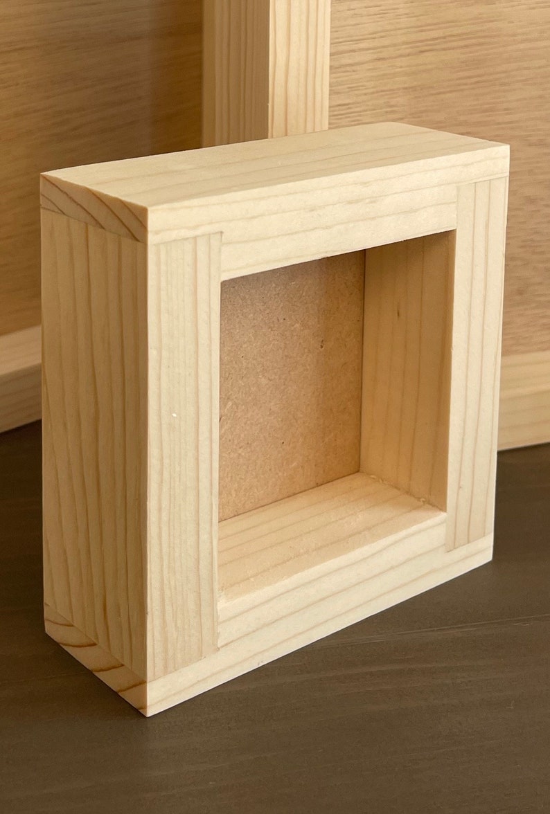 Puede incluir: Un peque&ntilde;o marco de fotos de madera sin terminar con un acabado de madera natural. El marco tiene una abertura rectangular y est&aacute; hecho de madera maciza.