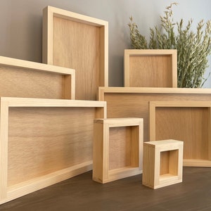 Puede incluir: Un conjunto de siete marcos de fotos de madera de diferentes tama&ntilde;os, todos hechos de madera natural con un acabado marr&oacute;n claro. Los marcos est&aacute;n dispuestos en forma escalonada sobre una superficie de madera.