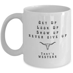 May include: White ceramic coffee mug with a black and white graphic design. The graphic features a skull with horns and the text "Get Up, Look Up, Show Up, Never Give Up, That's Western".