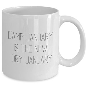 May include: White ceramic coffee mug with black text that reads "Damp January is the new Dry January".