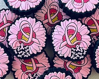 May include: A collection of pink flower-shaped charms with a pink ribbon design, symbolizing breast cancer awareness. The charms have a black border and a yellow center, creating a contrast against the light background.