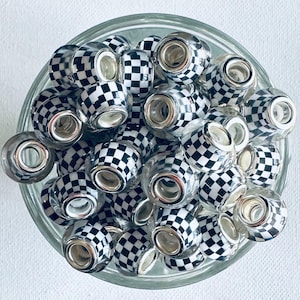 May include: A collection of clear glass beads with a silver-colored core and a black and white checkered pattern. The beads are contained in a clear glass bowl, viewed from above.