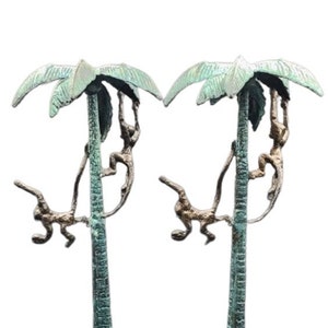 May include: A pair of bronze palm tree sculptures with monkeys climbing the trunks. The palm trees have green leaves and the monkeys are in a bronze finish.
