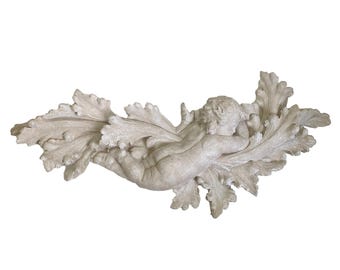 May include: A light-colored, decorative wall sculpture featuring a cherub figure reclining on a bed of large, stylized leaves. The sculpture is made of a solid material and has a matte finish. The cherub is seen from the back.