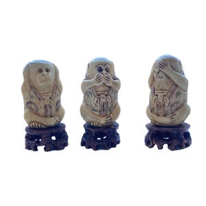 May include: Three beige monkey figurines, each in a different pose: covering eyes, mouth, and ears. The monkeys are on dark brown wooden stands. The figurines have detailed carvings and are a classic representation of the "See No Evil, Hear No Evil, Speak No Evil" concept.