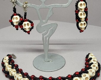 May include: A set of skull bead jewelry featuring a bracelet and earrings. The bracelet is made with black and red beads and white skull beads. The earrings are made with black and red beads and white skull beads.