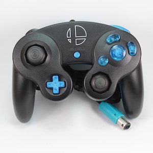May include: Black video game controller with blue detailing, including buttons and a connector. The controller features the "Super Smash Bros." logo in white. The controller has a classic design with a joystick, directional pad, and multiple buttons.