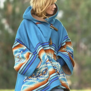 May include: A hooded blue poncho with a Southwestern-inspired pattern in shades of orange, blue, and white. The poncho features a toggle closure and a brown lining. The sleeves and hood are adorned with the geometric design.