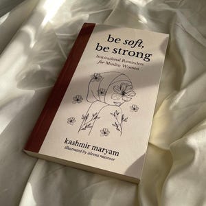 May include: A book titled "be soft, be strong" with a line drawing of a woman wearing a headscarf and flowers. The subtitle is "Inspirational Reminders for Muslim Women". The book is by kashmir maryam and illustrated by aleena masroor.