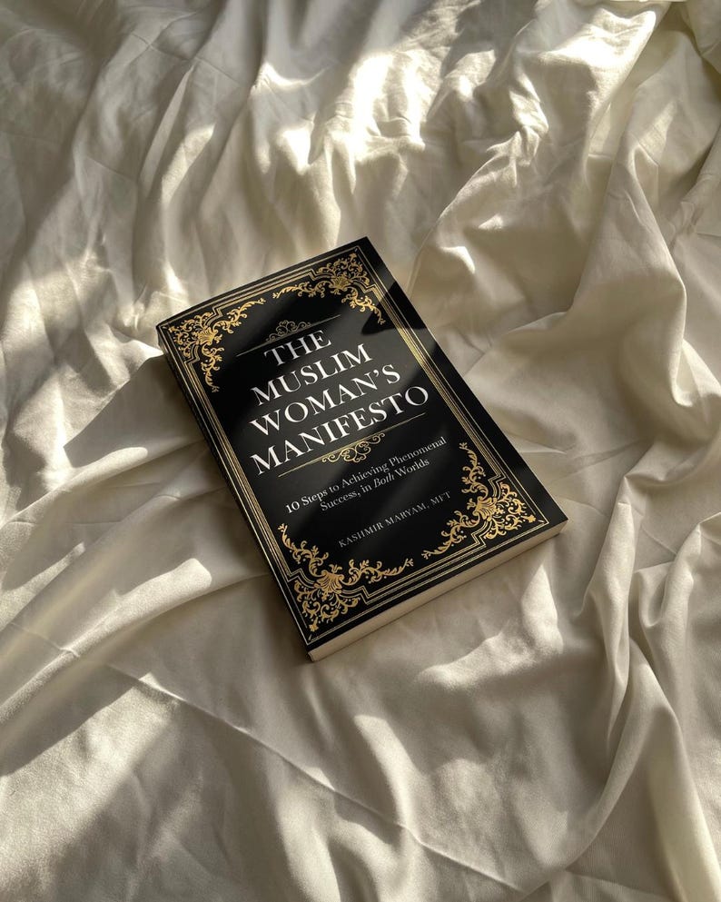 May include: A black book with gold lettering titled "The Muslim Woman's Manifesto: 10 Steps to Achieving Phenomenal Success, in Both Worlds" by Kashmir Maryam, MIT.