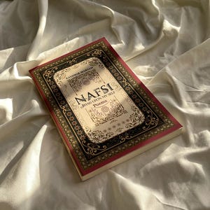 May include: A book titled "NAFSI: JIHAD UPON MY SELF Poems" by Kashimik Makyam. The book cover features an ornate, gold and black frame with intricate floral designs.
