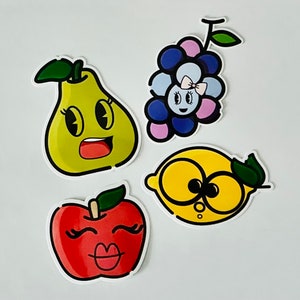 May include: Four colorful cartoon fruit stickers with faces. A yellow pear, a red apple, a yellow lemon, and a purple grape cluster.