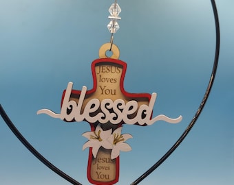 May include: A wooden cross ornament with a red border and the words "JESUS loves You" and "blessed" in white. The cross features a floral design and is suspended by a beaded wire.