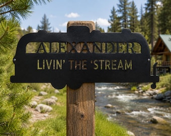 May include: A black metal sign shaped like a vintage travel trailer mounted on a wooden post. The sign features the cut-out text ALEXANDER on the top line and the text LIVIN' THE 'STREAM on the bottom line in a bold, sans-serif font.