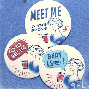 May include: Three circular pinback buttons with white backgrounds. One reads MEET ME IN THE GROVE. Another features a red speech bubble saying GO TO HELL LSU. The third has a light blue speech bubble saying BEAT LS WHO! Each shows a stylized person holding a red cup.