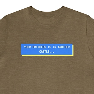May include: A brown t-shirt with a blue and yellow rectangle on the front. The rectangle contains the text "YOUR PRINCESS IS IN ANOTHER CASTLE..."