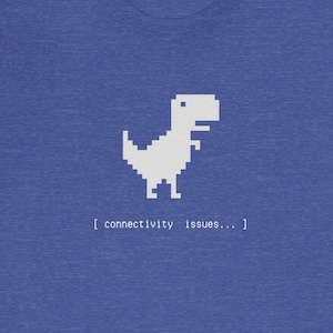 Puede incluir: Una camiseta azul con un dinosaurio pixelado blanco y el texto "[connectivity issues... ]" impreso en ella.