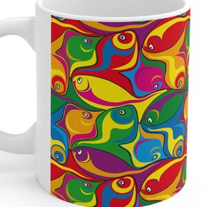 May include: White ceramic mug with a colorful pattern of abstract fish. The fish are in shades of red, orange, yellow, green, blue, and purple.