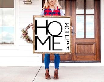 May include: A white wooden sign with the words "Home sweet Home" in black lettering. The letters are stylized and the word "Home" is in large, bold letters. The sign is being held by a person in front of a white house.