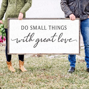 Puede incluir: Una pareja sostiene un cartel blanco con el texto "DO SMALL THINGS with great love" escrito en negro. El cartel se sostiene frente a un campo con nieve y hierba verde.