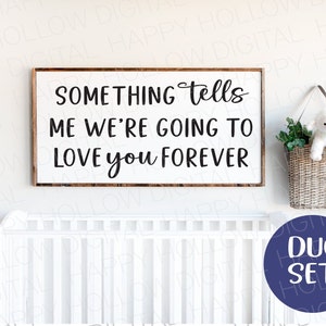 Puede incluir: Un letrero de madera enmarcado con el texto "SOMETHING tells ME WE'RE GOING TO LOVE YOU FOREVER" en escritura negra. Una cesta tejida con un cordero de peluche y vegetación cuelga cerca. Un círculo azul con "DUO SET" está en la parte inferior derecha.