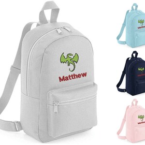 May include: A grey, personalised backpack with a green dragon and the name "Matthew" embroidered on the front. The backpack has two zipped compartments and adjustable straps.