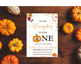 May include: A birthday invitation with a pumpkin theme. The invitation reads "Our little Pumpkin is turning ONE." The invitation is surrounded by small pumpkins and gourds on a wooden surface. The invitation includes the date, time, and RSVP information.