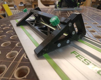 May include: A black and silver woodworking guide with green accents and adjustable knobs. The guide is positioned on a silver track with green stripes and the word "FESTOOL" in green. The tool is designed for precision cutting.