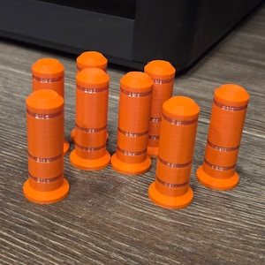 May include: Eight orange cylinders with a flat base and a rounded top. Each has two thin, horizontal, light-coloured bands. They are arranged on a wooden surface. Each cylinder is approximately 5 cm tall.