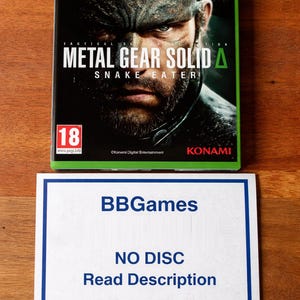 Può includere: Custodia del gioco Metal Gear Solid Δ: Snake Eater Day One Edition per Xbox Series X. La copertina presenta un primo piano del volto di un uomo con il titolo e il logo del gioco. Un cartello bianco sottostante recita "BBGames NO DISC Read Description."