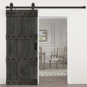 May include: A dark gray wooden sliding barn door with a black metal track and hardware. The door has three horizontal panels with decorative metal accents. The door is open, revealing a room with a white rug and furniture.