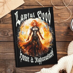 May include: A black notebook with the text "Lawful Good Honor & Righteousness" in white lettering. The cover features a digital illustration of a woman in armor standing in a circle of fire.