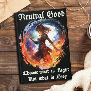 Puede incluir: Una libreta negra con una ilustración colorida de una persona con el pelo suelto de pie en un círculo de fuego y agua. El texto "Neutral Good" está en la parte superior de la libreta y el texto "Choose what is Right Not what is Easy" está en la parte inferior.