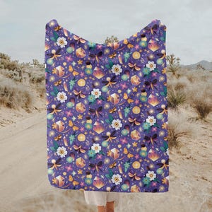 Puede incluir: Manta de forro polar morada con un patrón caprichoso de mariposas, flores y cristales. El patrón está en tonos de morado, rosa, amarillo y verde.