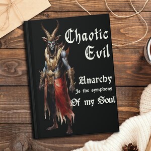 Può includere: Un libro nero con un'illustrazione di un demone sulla copertina. Il testo sulla copertina recita "Chaotic Evil Anarchy is the symphony of my Soul".
