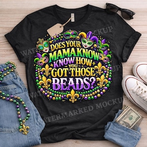 May include: Dark grey t-shirt featuring a vibrant Mardi Gras design with masks, fleur-de-lis, and the text "DOES YOUR MAMA KNOW HOW YOU GOT THOSE BEADS?". Sunglasses, a tag, and white trainers are also visible.